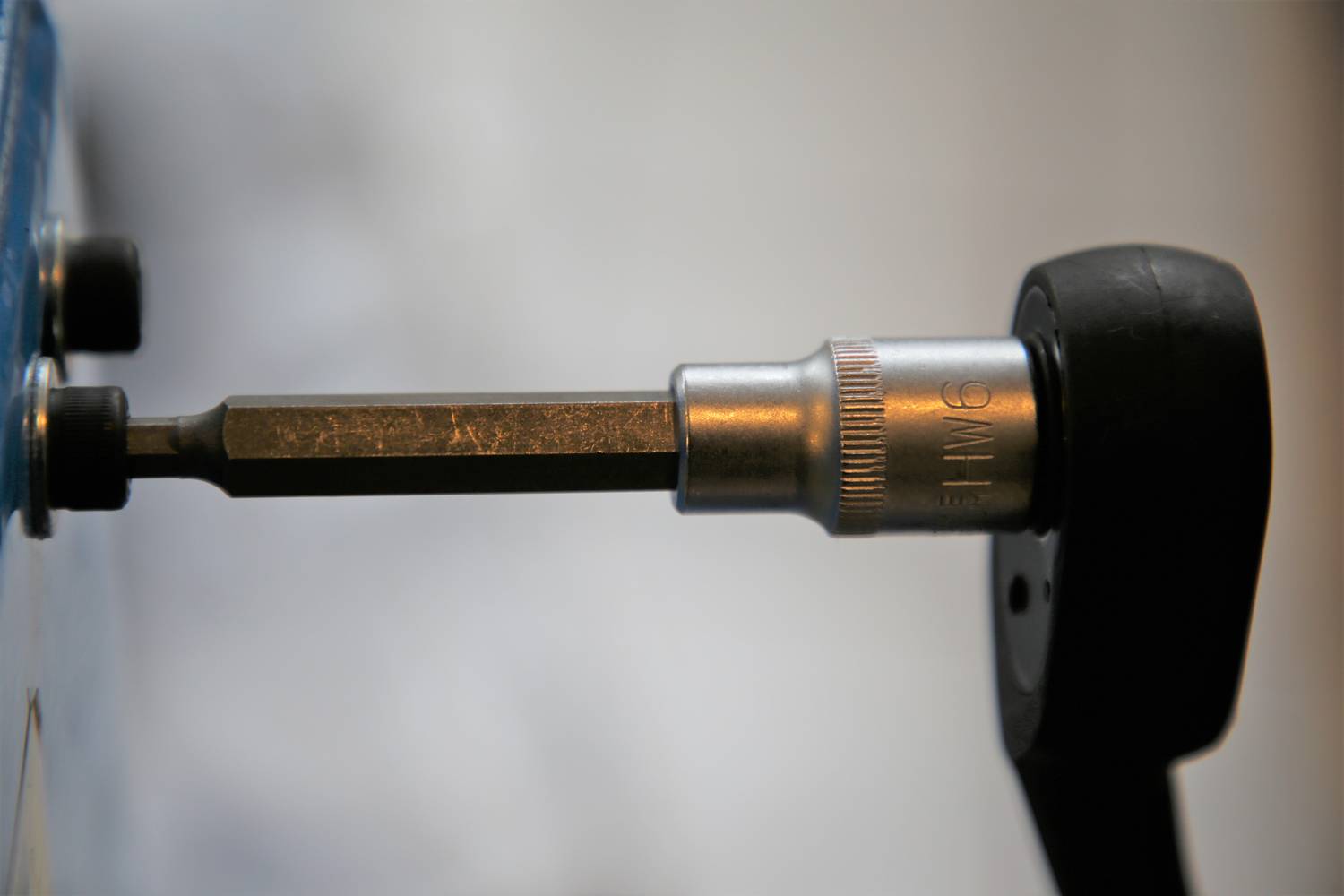 Zbliżenie zestawu kluczy nasadowych z adapterem sześciokątnym włożonym w łeb śruby na rozmytym tle.