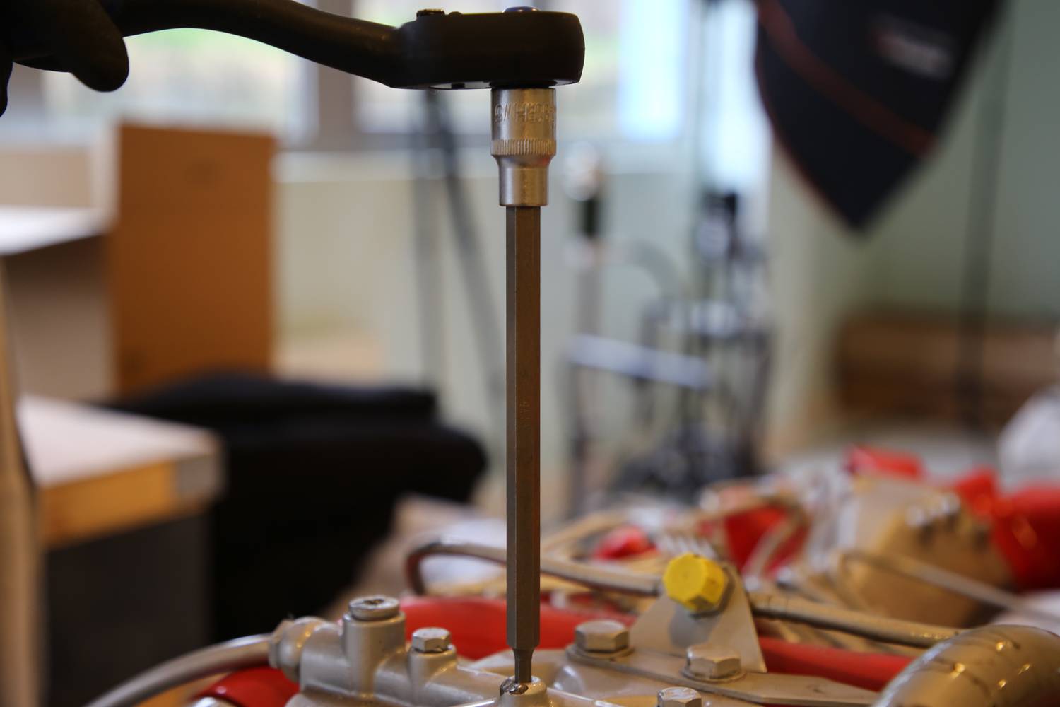 Osoba dokręca śrubę kluczem w maszynie. W tle rozmyte pomieszczenie laboratoryjne.