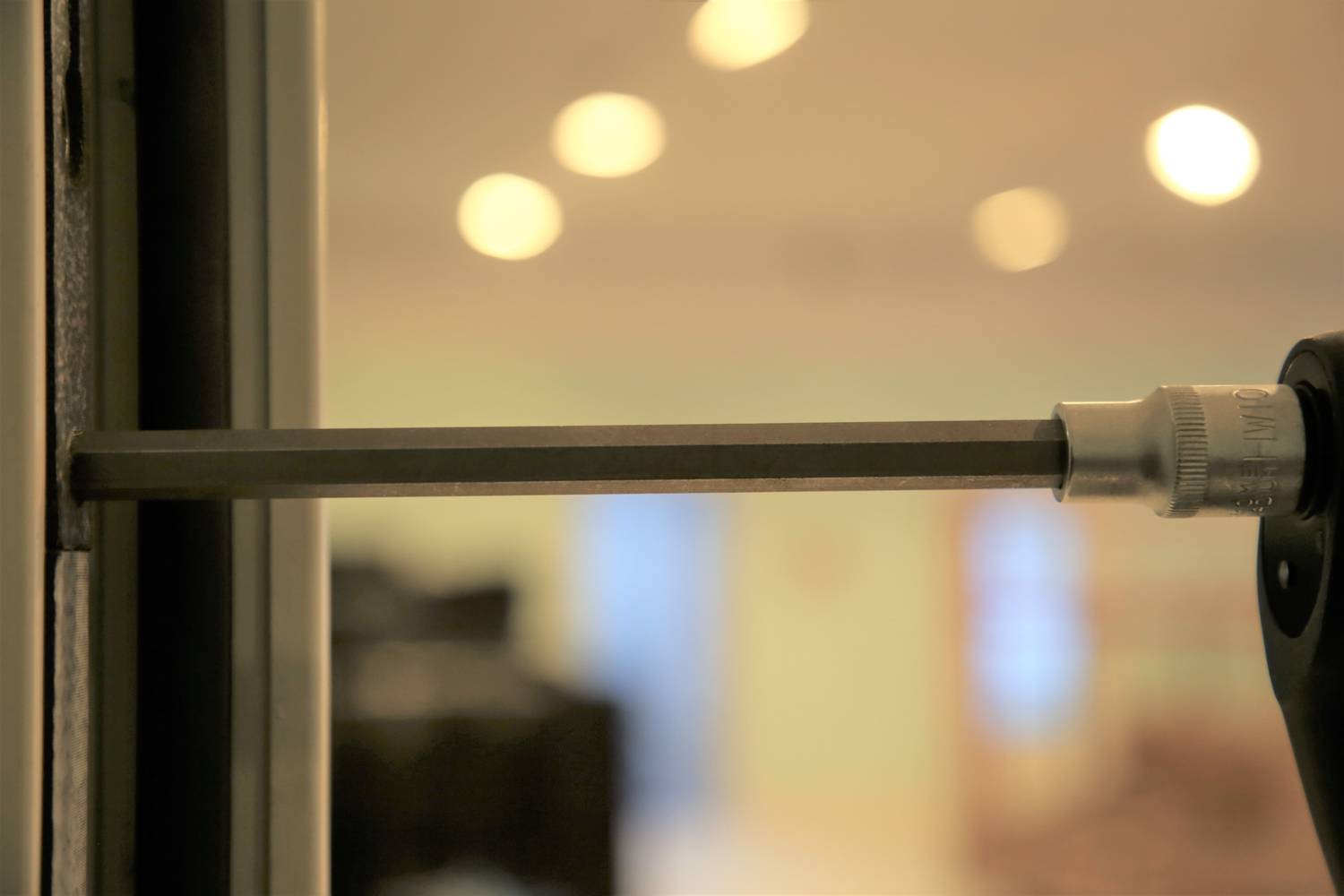 Wkrętak wkręca śrubę w metalową powierzchnię. Tło jest rozmyte i ukazuje scenę wnętrza.