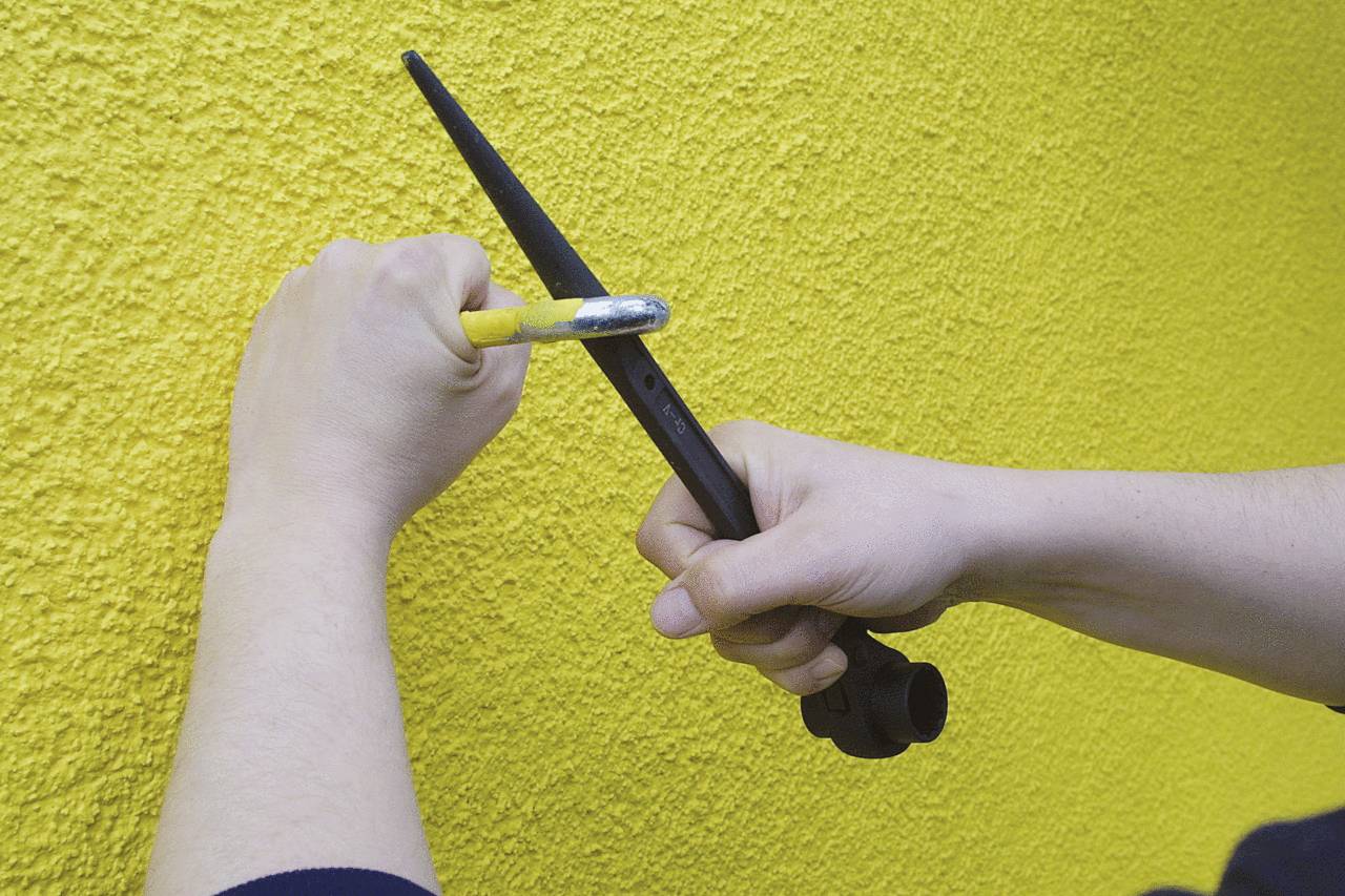 Przewiercanie ściany narzędziem na żółtej, strukturalnej powierzchni. Dwie ręce trzymają narzędzia, aby wywiercić otwór w ścianie.