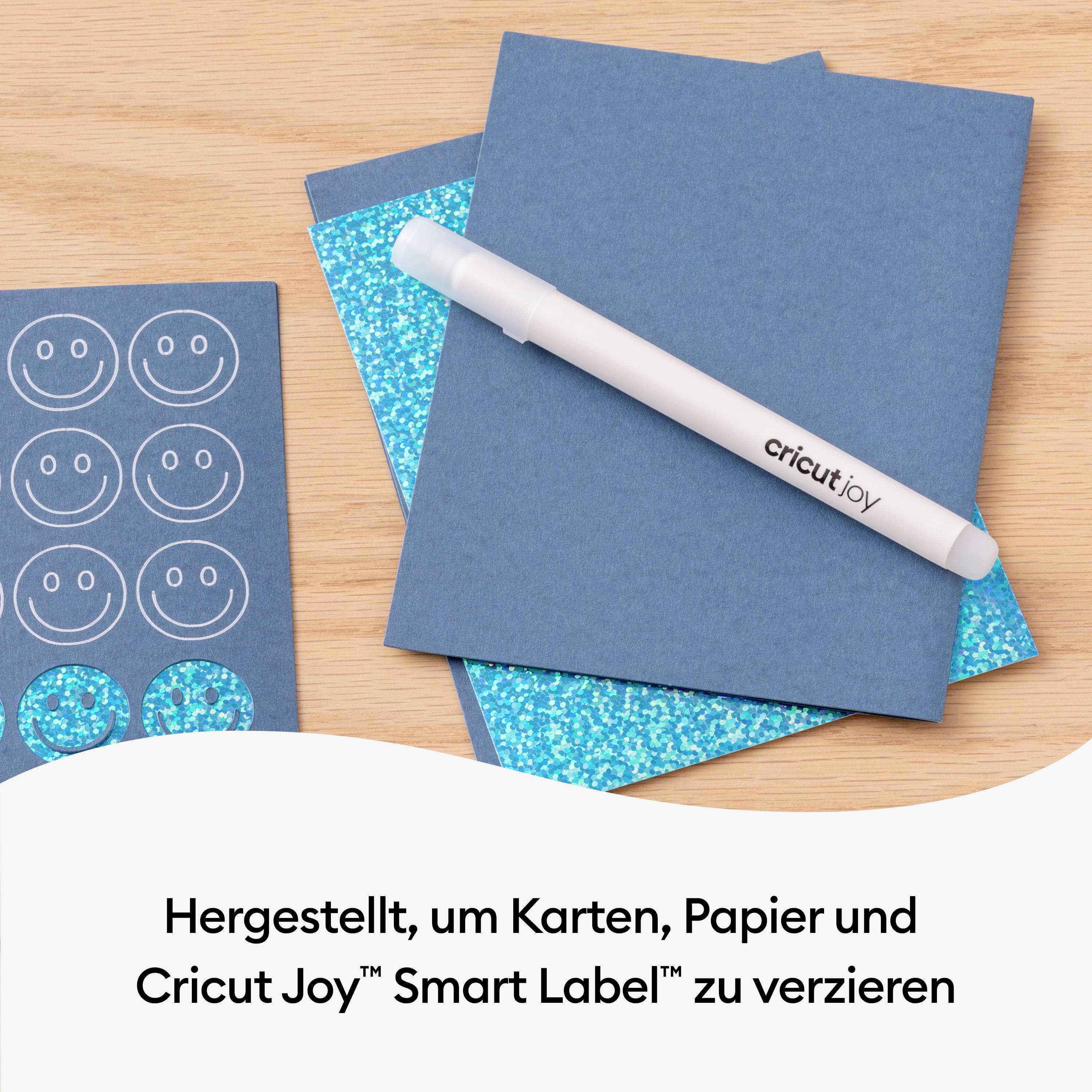 Kartki i materiały papiernicze na drewnianym stole, z piórem Cricut Joy i napisem "Stworzono, aby ozdobić kartki, papier i etykiety Cricut Joy™ Smart Label™".