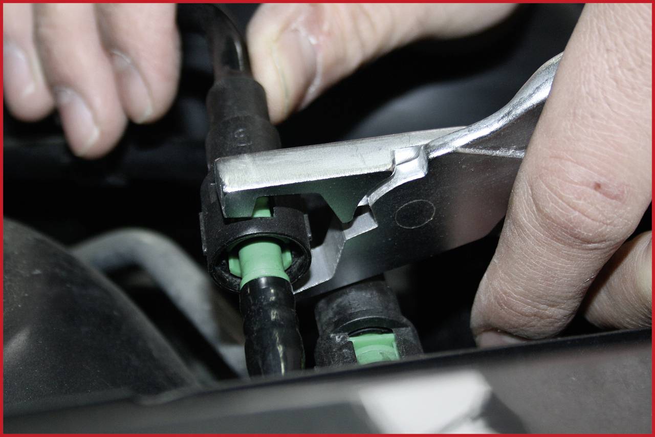 Zbliżenie dłoni, która za pomocą szczypiec odpina złącze przewodu w samochodzie.