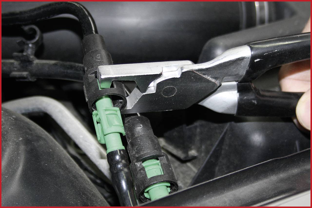 Zbliżenie narzędzia trzymającego zielony złącz w obszarze komponentów silnika, prawdopodobnie podczas naprawy lub konserwacji.