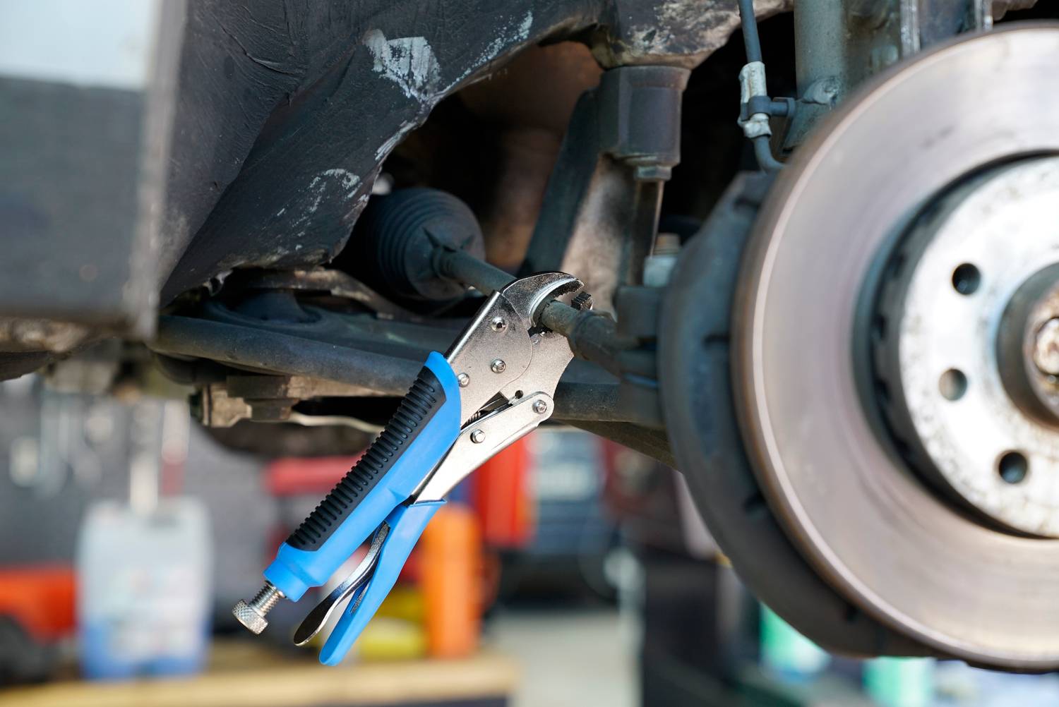 Szczypce trzymają śrubę na podwoziu samochodu obok tarczy hamulcowej. Mechaniczna praca naprawcza w warsztacie.