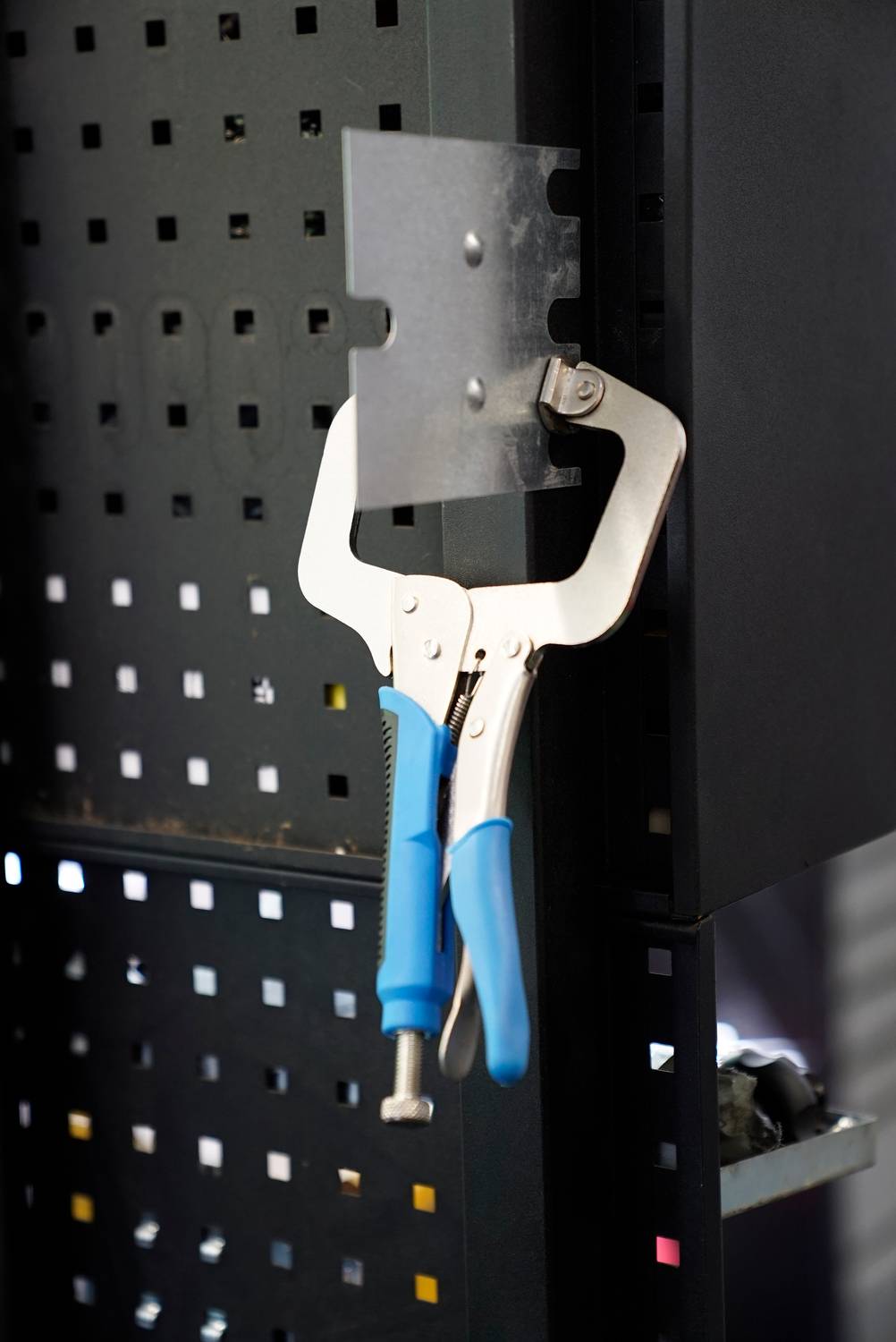 Zacisk z niebieskimi uchwytami wisi na metalowej kratce.