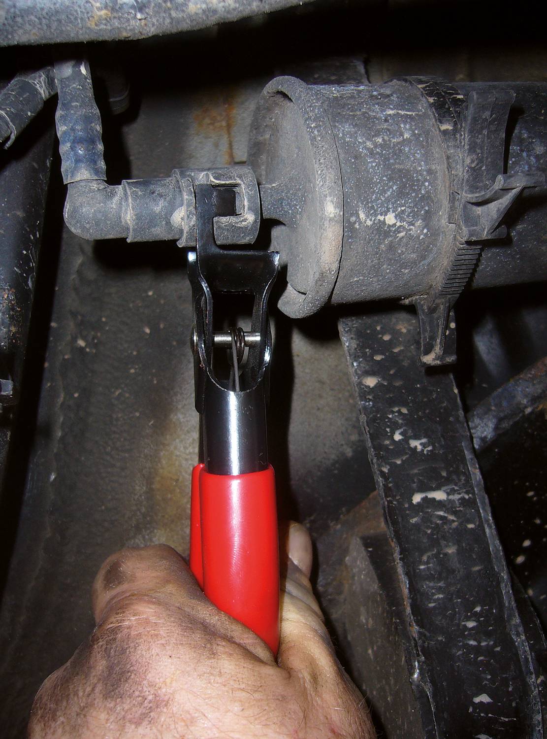 Mechanik używa szczypiec, aby zabezpieczyć złącze przewodu w pojeździe. Przewód i otoczenie są zakurzone.