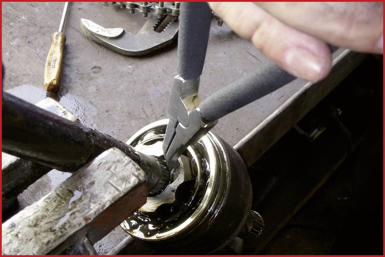 Osoba naprawia złączkę części maszyny za pomocą szczypiec na stole warsztatowym, otoczona różnymi narzędziami.