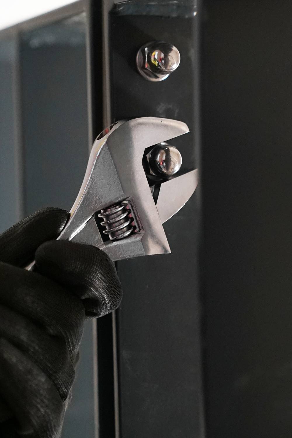 Dłoń w czarnej rękawicy używa regulowanego klucza do dokręcenia śruby w elemencie metalowym.