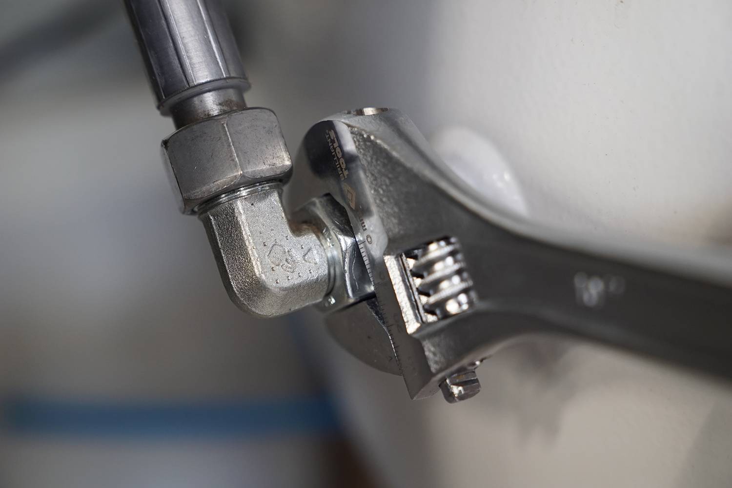 Zbliżenie nastawnego klucza francuskiego obracającego się wokół srebrnego złącza rurowego. Fokus na narzędziu i mocowaniu.