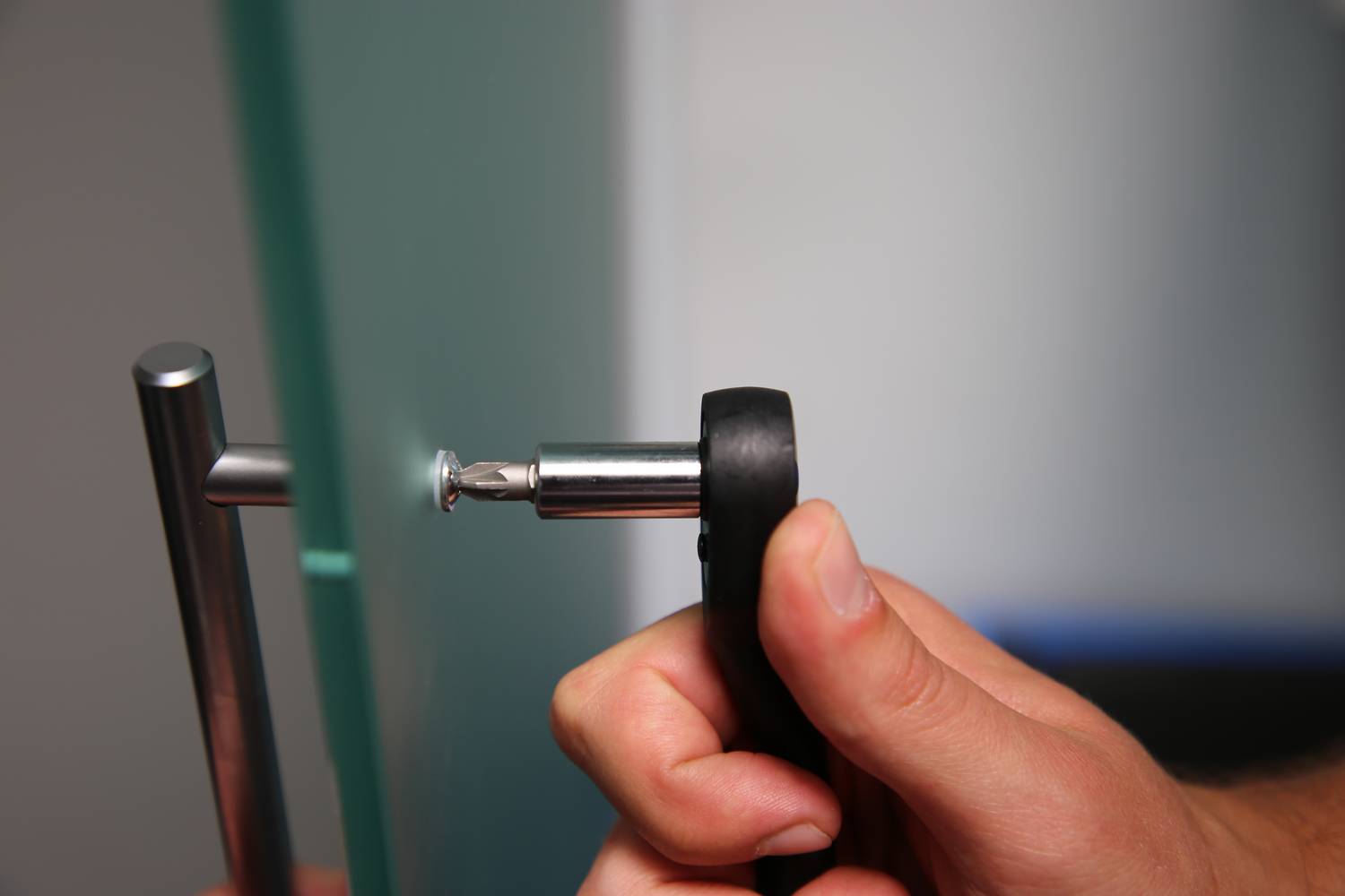 Ręka używa klucza imbusowego do dokręcenia śruby w klamce drzwi.