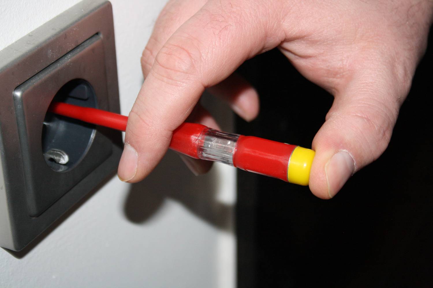 Ręka wkłada czerwony kabel sieciowy do szarego gniazda ściennego.