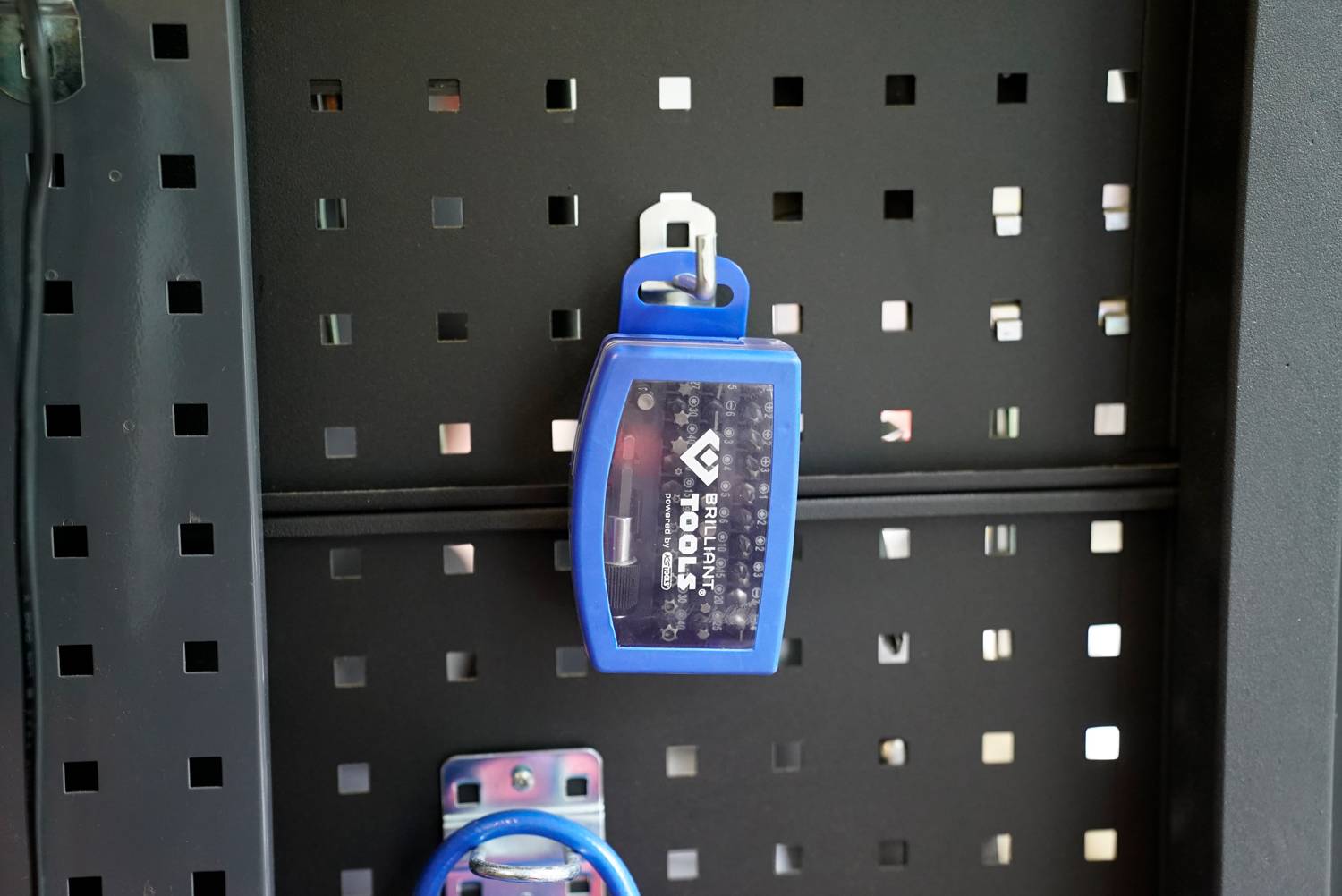 Niebieski sejf na klucze wisi na czarnej tablicy perforowanej.