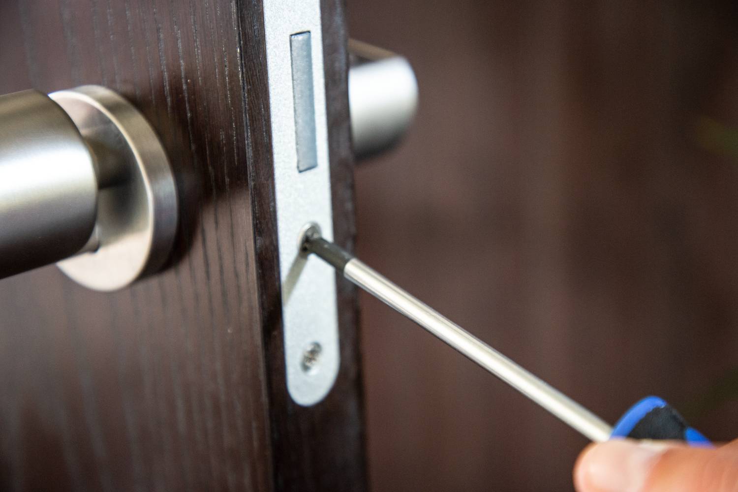 Ręka przykręca wkrętakiem zamek do drewnianych drzwi.