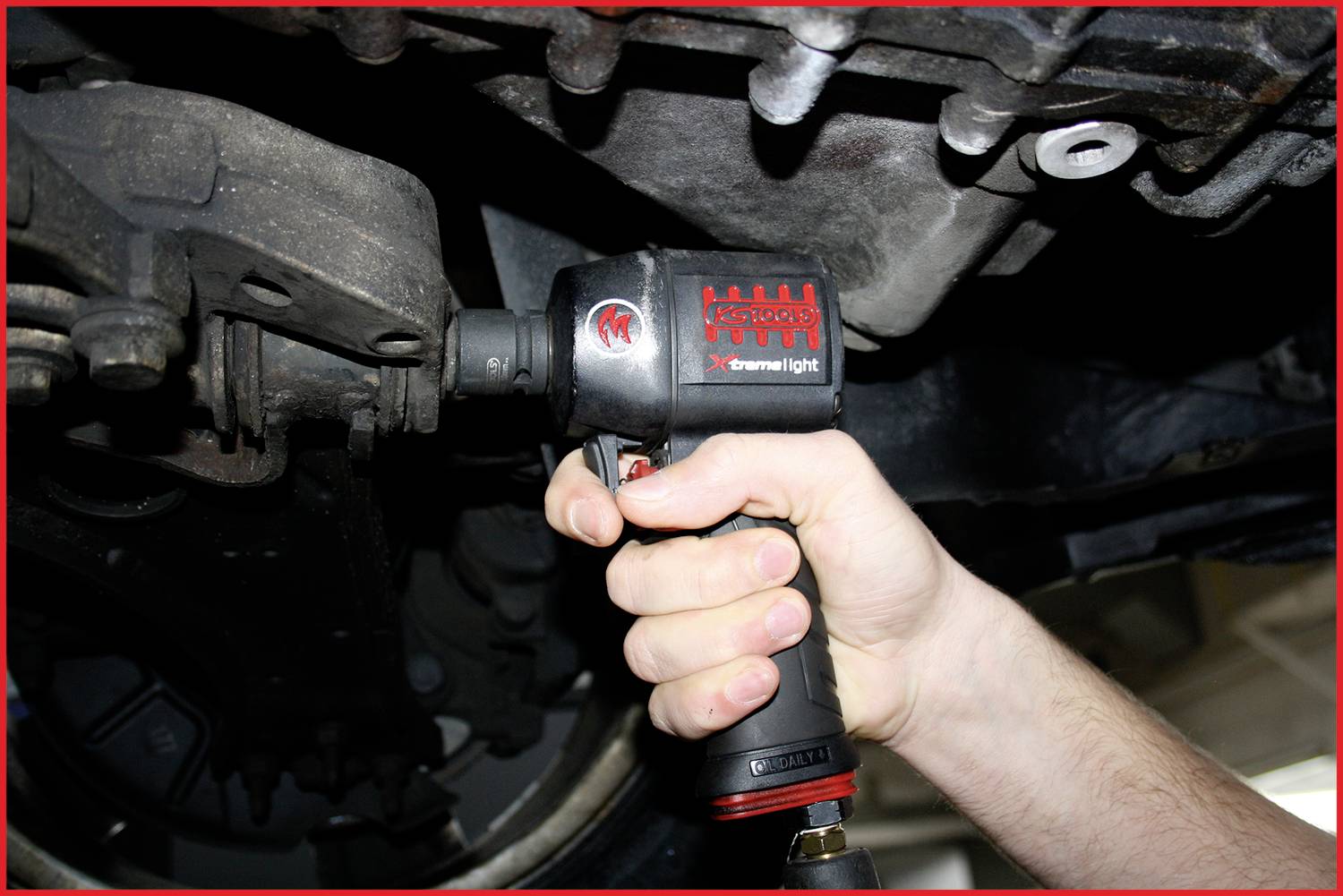 Osoba naprawia samochód, używając klucza udarowego do pracy przy śrubie. Fokus jest skierowany na dłoń i narzędzie.