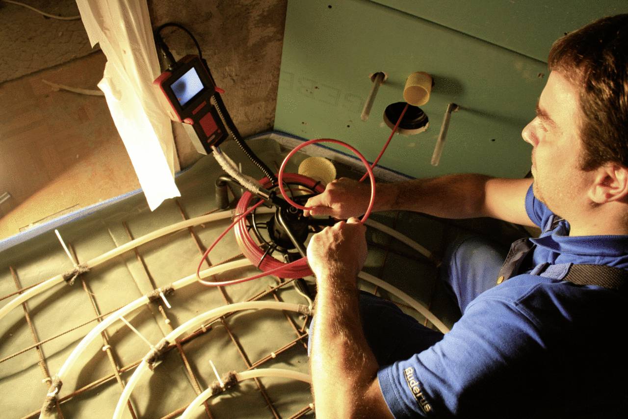 Technik sprawdza rury systemu ogrzewania podłogowego za pomocą kamery. Na ekranie monitoruje przebieg przewodów.