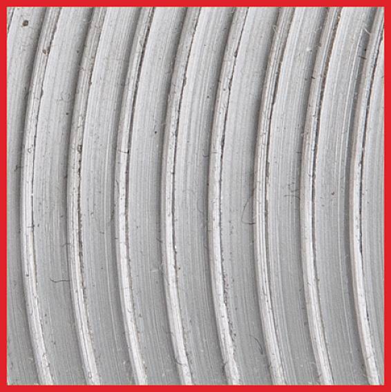 Zbliżenie srebrnych, koncentrycznych rowków na metalowej powierzchni w czerwonej ramce.