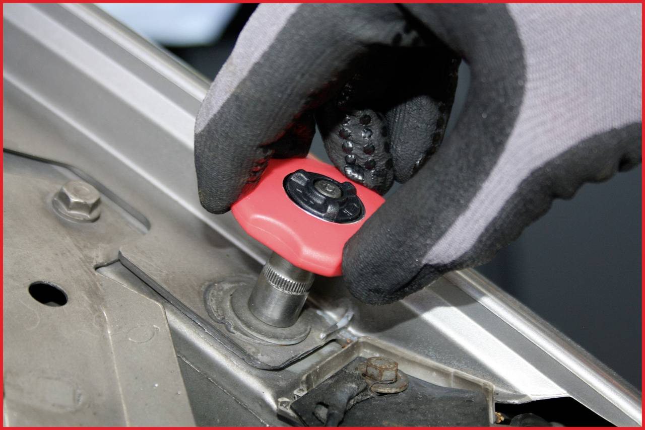 'Dłoń w rękawicy używa czerwonego narzędzia do dokręcenia nakrętki na metalowej powierzchni.'