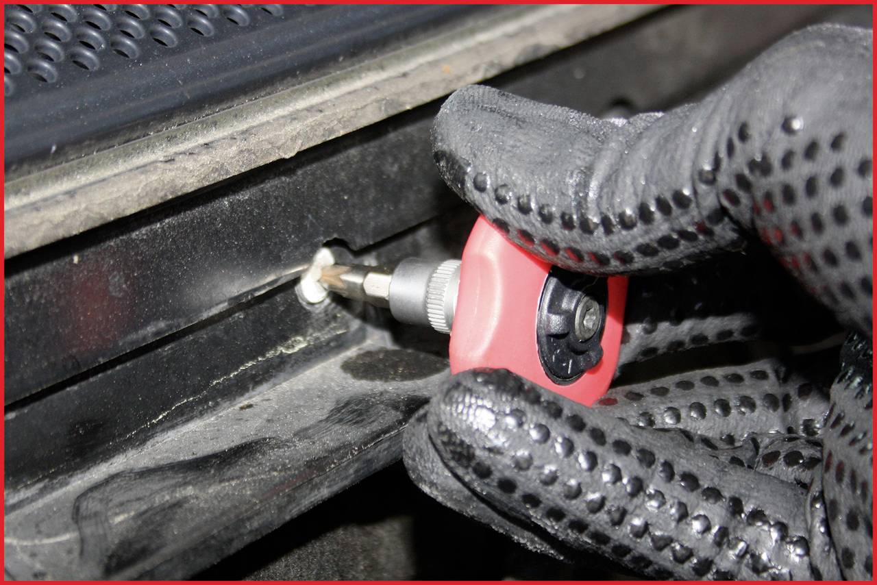 Zbliżenie dłoni w rękawicy roboczej, która pracuje wkrętakiem na czarnej powierzchni.