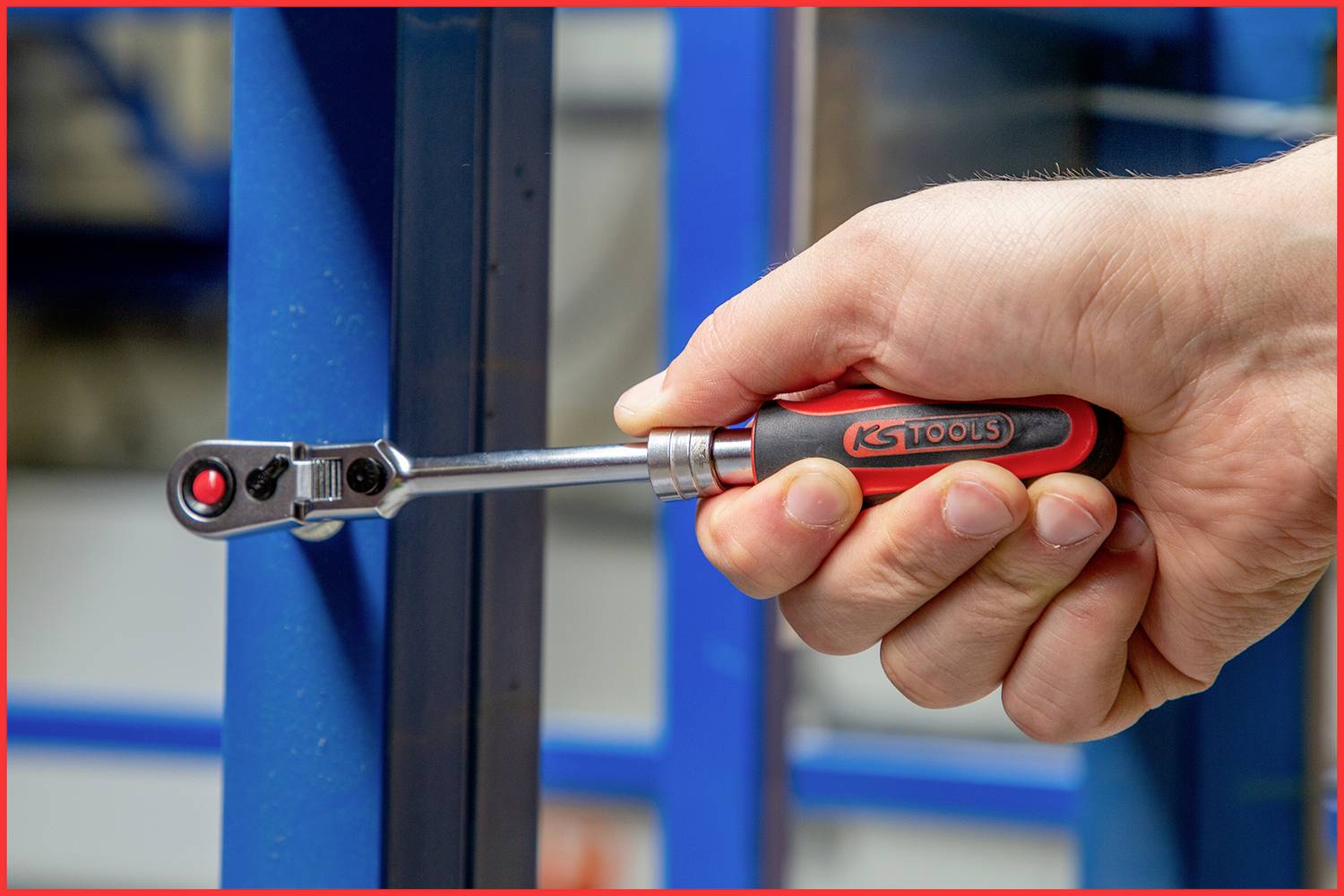 Jedna ręka trzyma klucz grzechotkowy KS Tools, który pracuje przy niebieskiej strukturze metalowej.