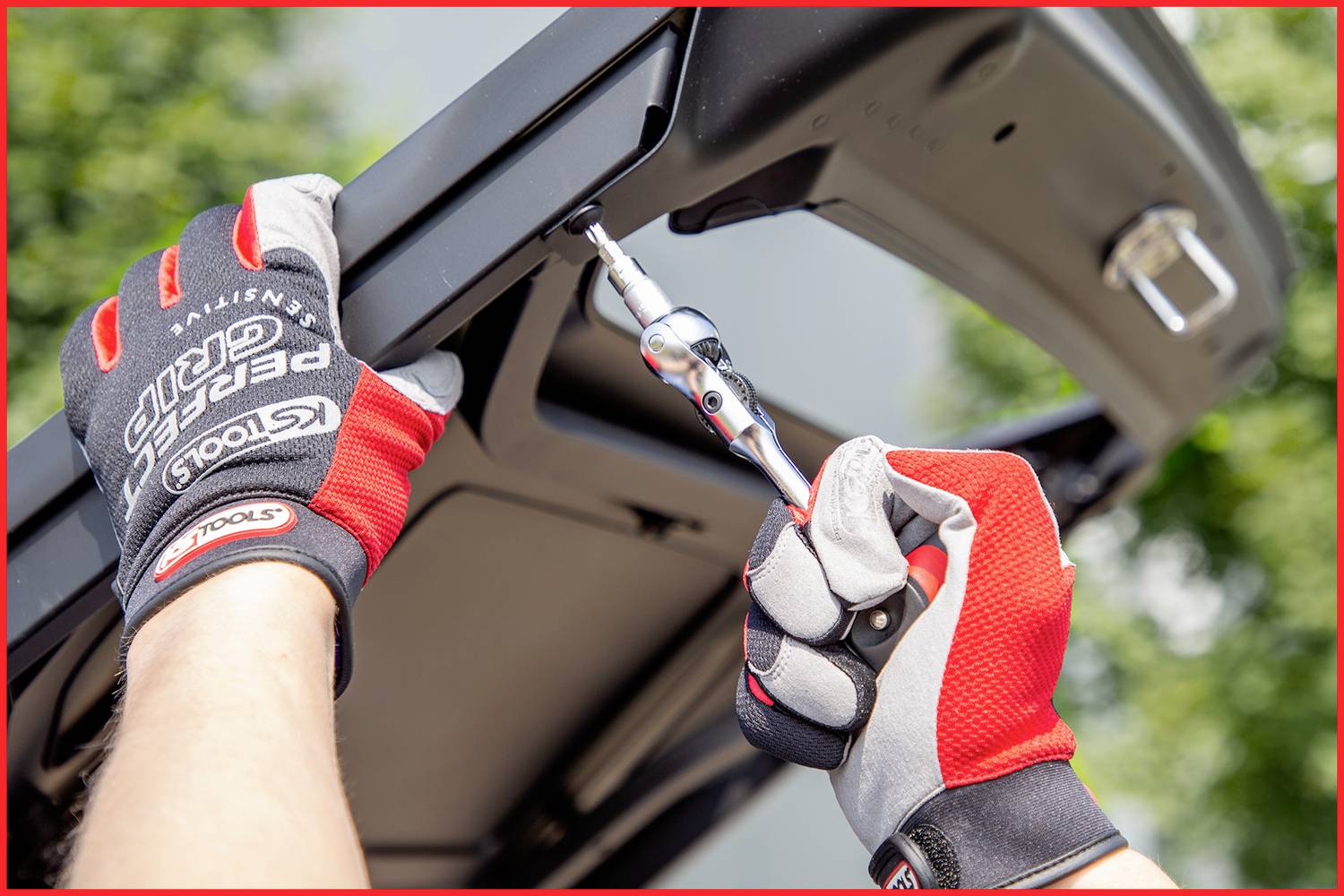 Osoba w rękawiczkach używa klucza do dokręcenia śruby przy tylnej części samochodu.