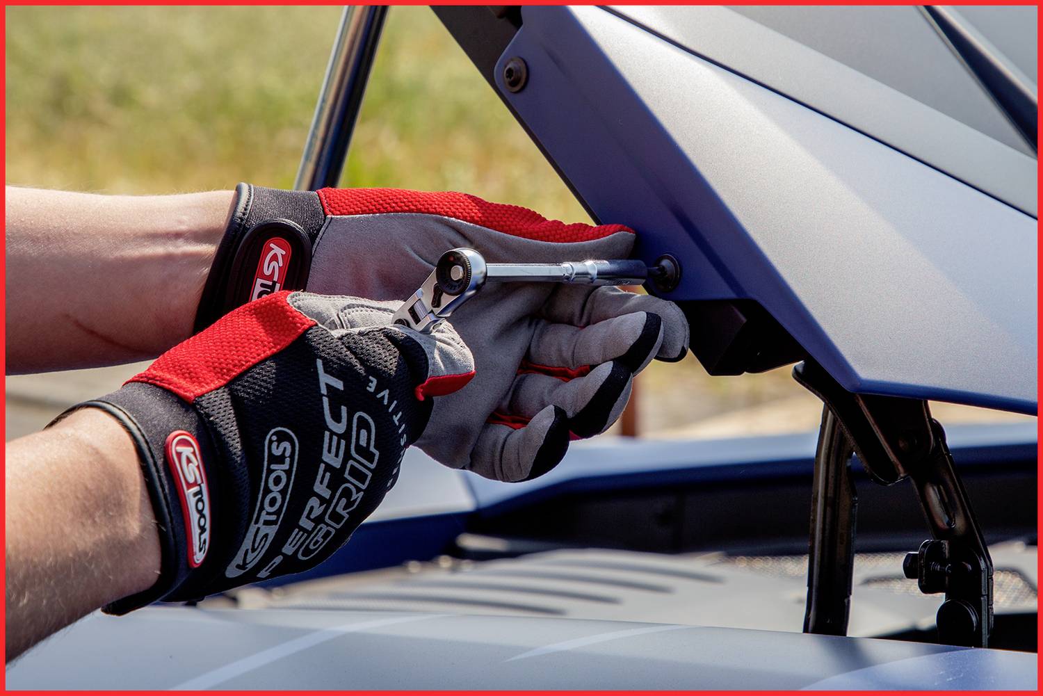 Mechanik w rękawicach dokręca śrubę na metalowej osłonie na dworze za pomocą klucza.