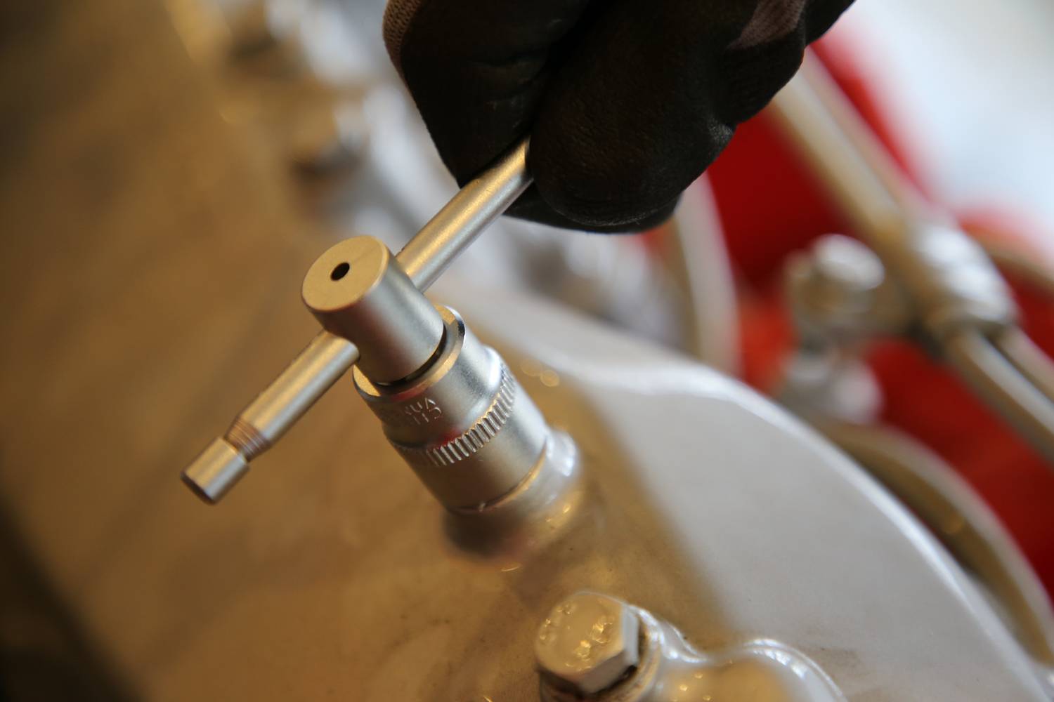 Dłoń w rękawicy trzyma narzędzie nad metalowym elementem wbudowanym w maszynę.