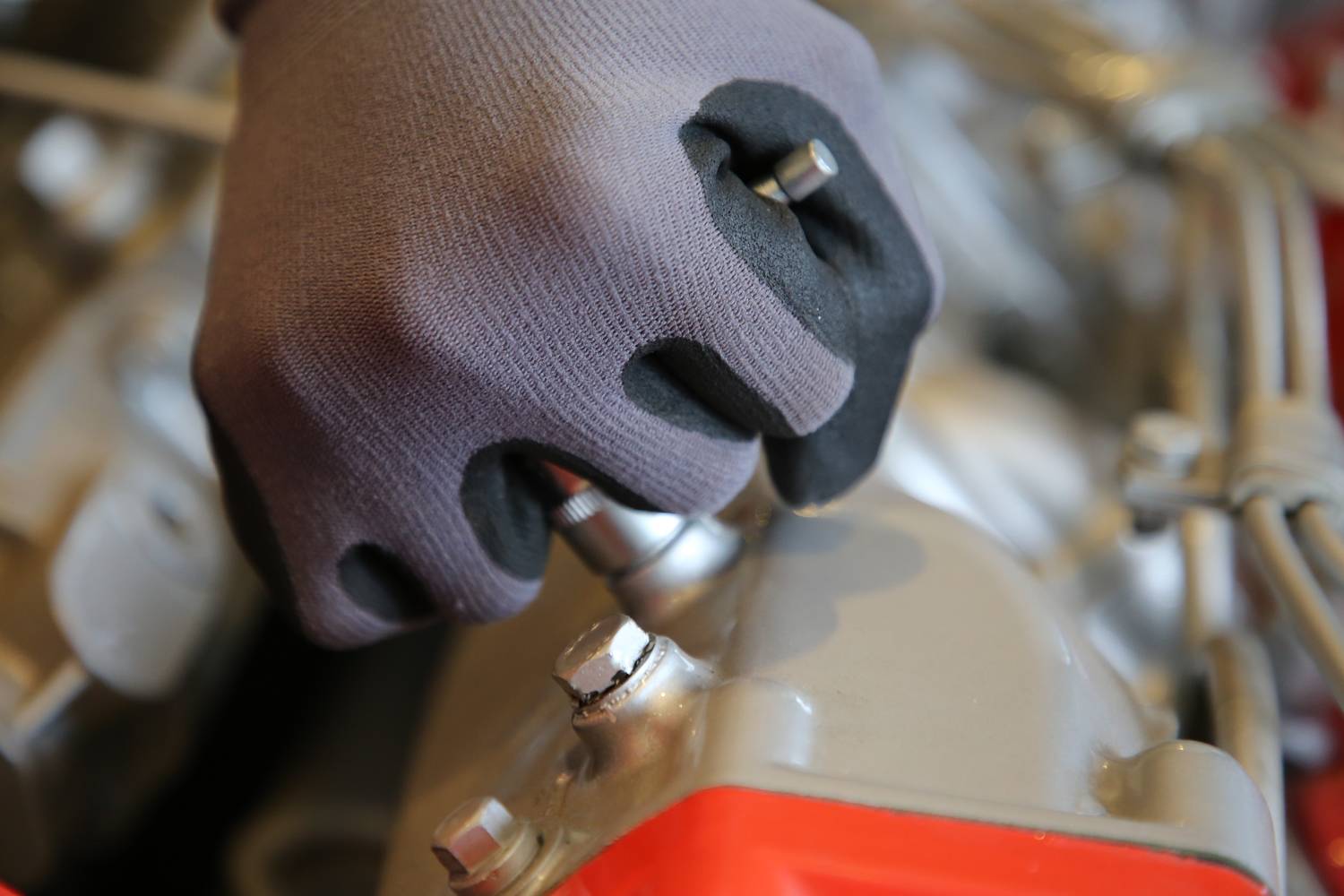 Dłoń w rękawicy roboczej dokręca śrubę w urządzeniu technicznym, z fokusem na ruch ręki i samą śrubę.