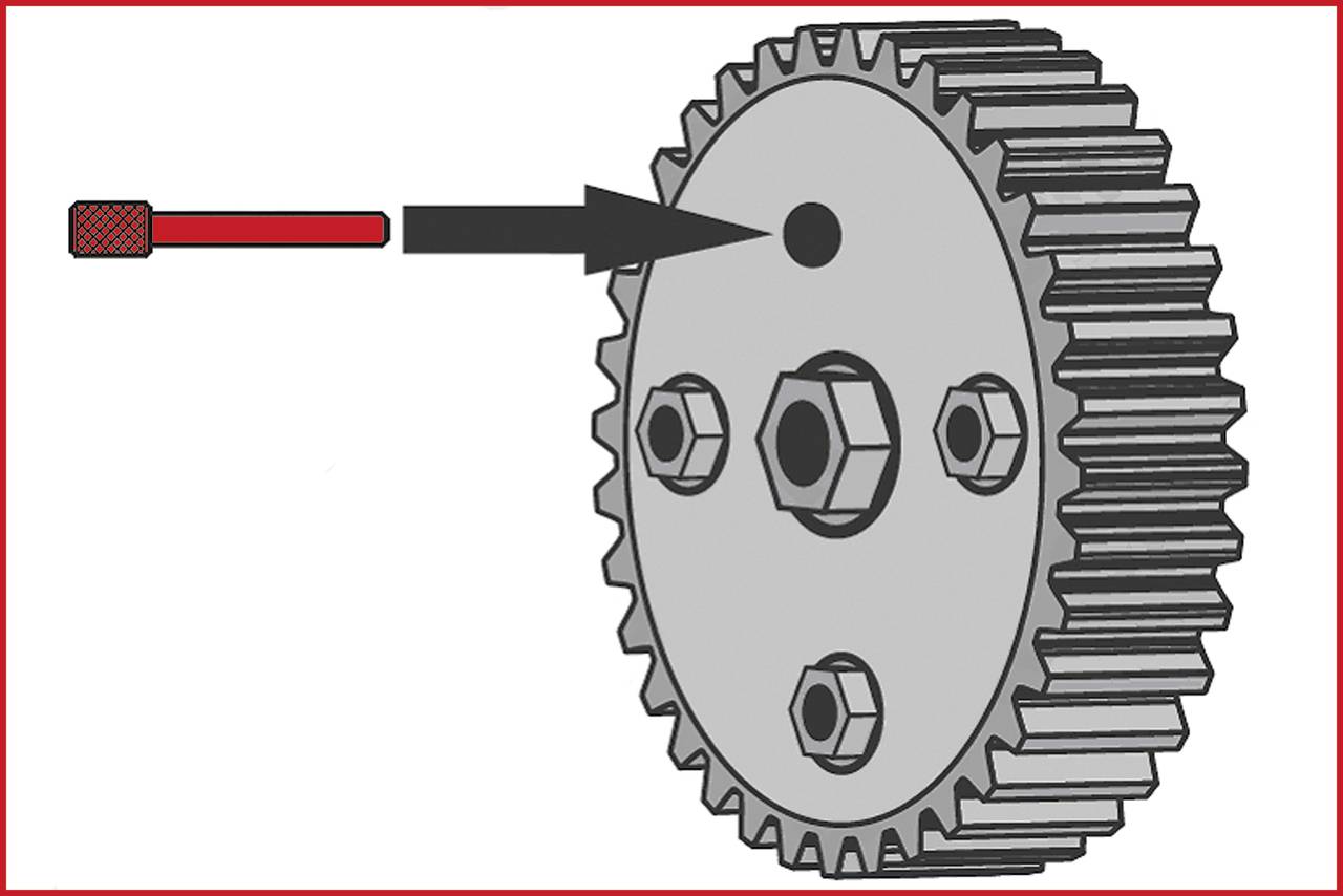 Koło zębate z strzałką wskazującą na określony punkt. Koło zębate posiada kilka otworów na śruby. Strzałka podkreśla konkretne miejsce.