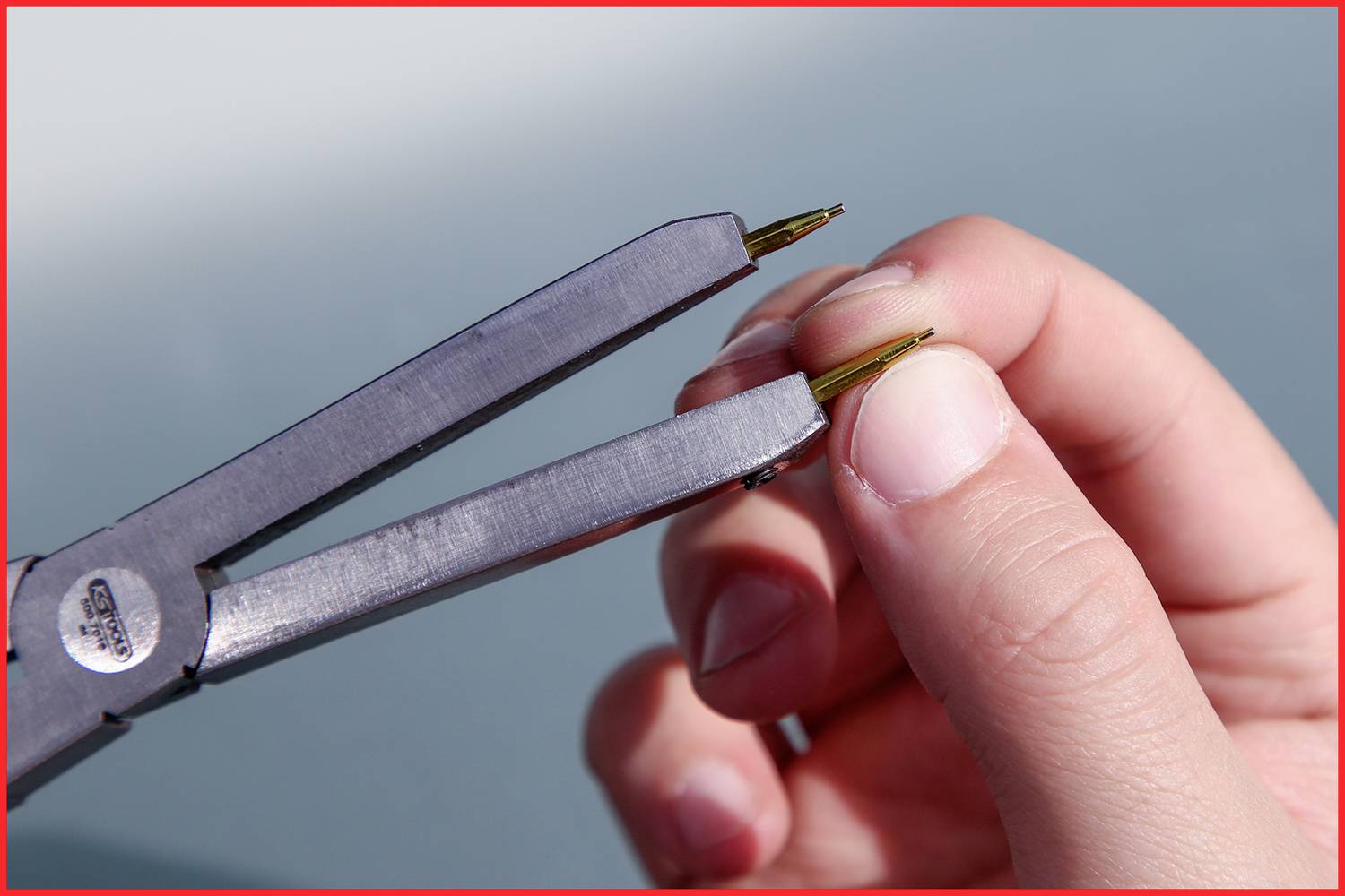 Jedna ręka trzyma pęsetę, która chwyta cienki drut. Pęseta jest stabilizowana przez drugą rękę.