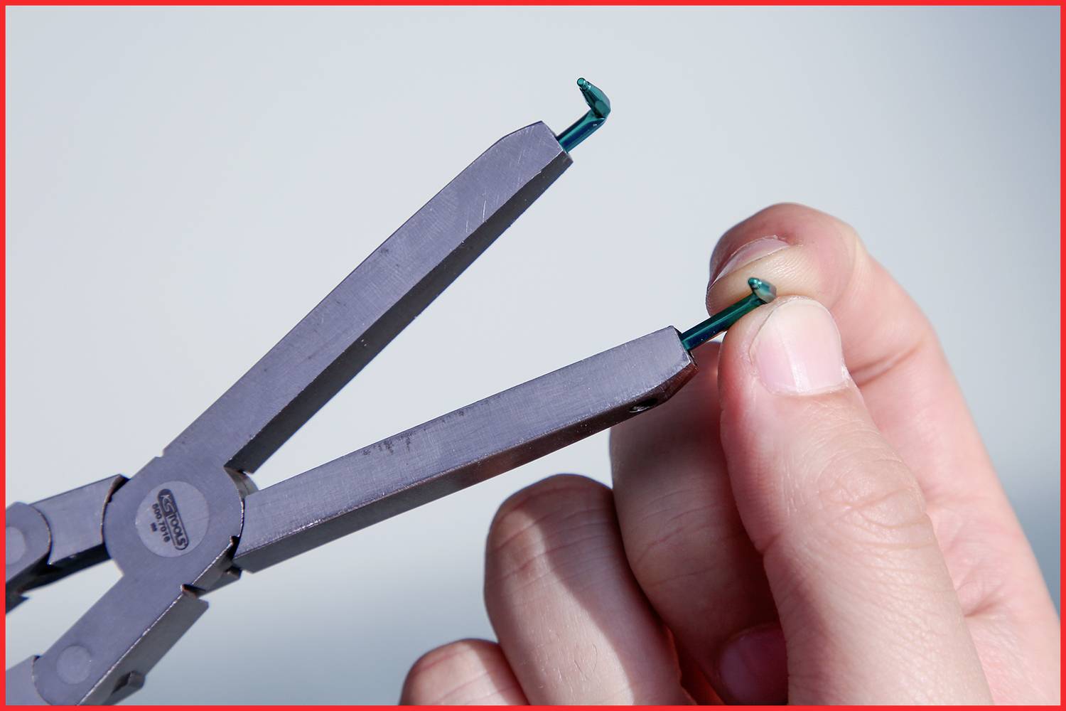 Ręka usuwa kolczyk z płatka ucha za pomocą szczypiec.