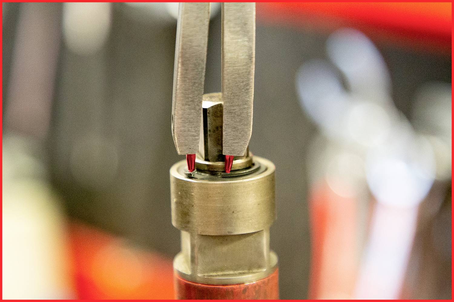 Dwie metalowe szczypce trzymają małą, cylindryczną część w warsztacie. Rozmyty tło sugeruje otoczenie.