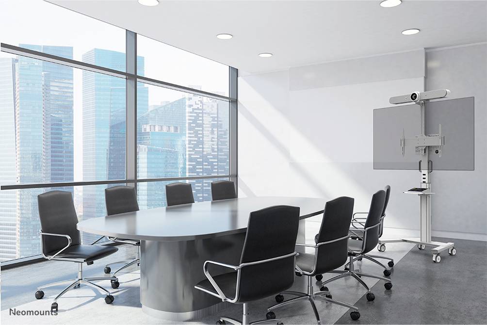 Sala konferencyjna z dużym owalnym stołem, otoczonym ośmioma czarnymi krzesłami. W tle duże okna z widokiem na miasto, po prawej stronie ekran.