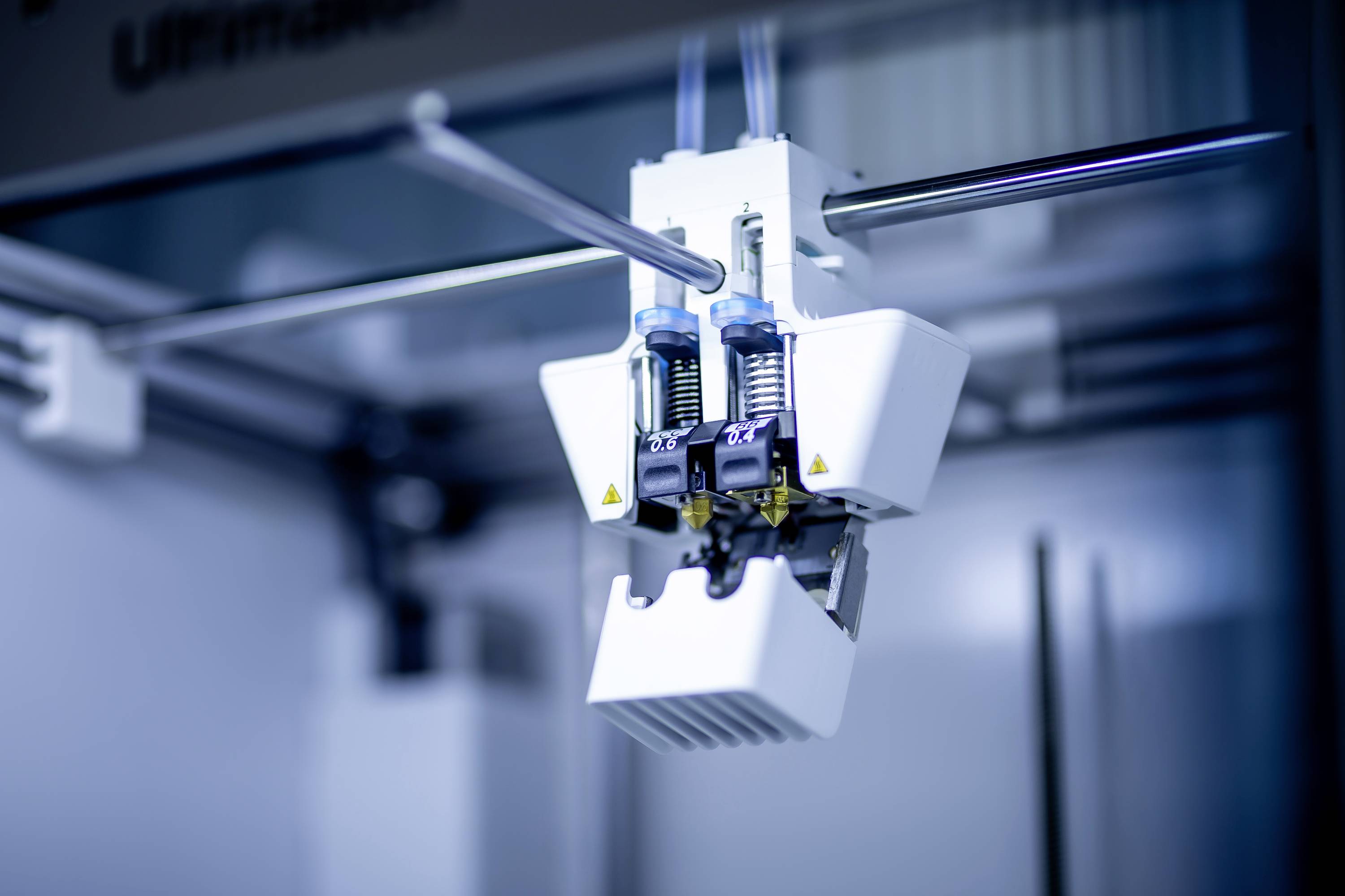 Zbliżenie działającego ekstrudera drukarki 3D nakładającego warstwę materiału plastikowego. Tło jest rozmyte.