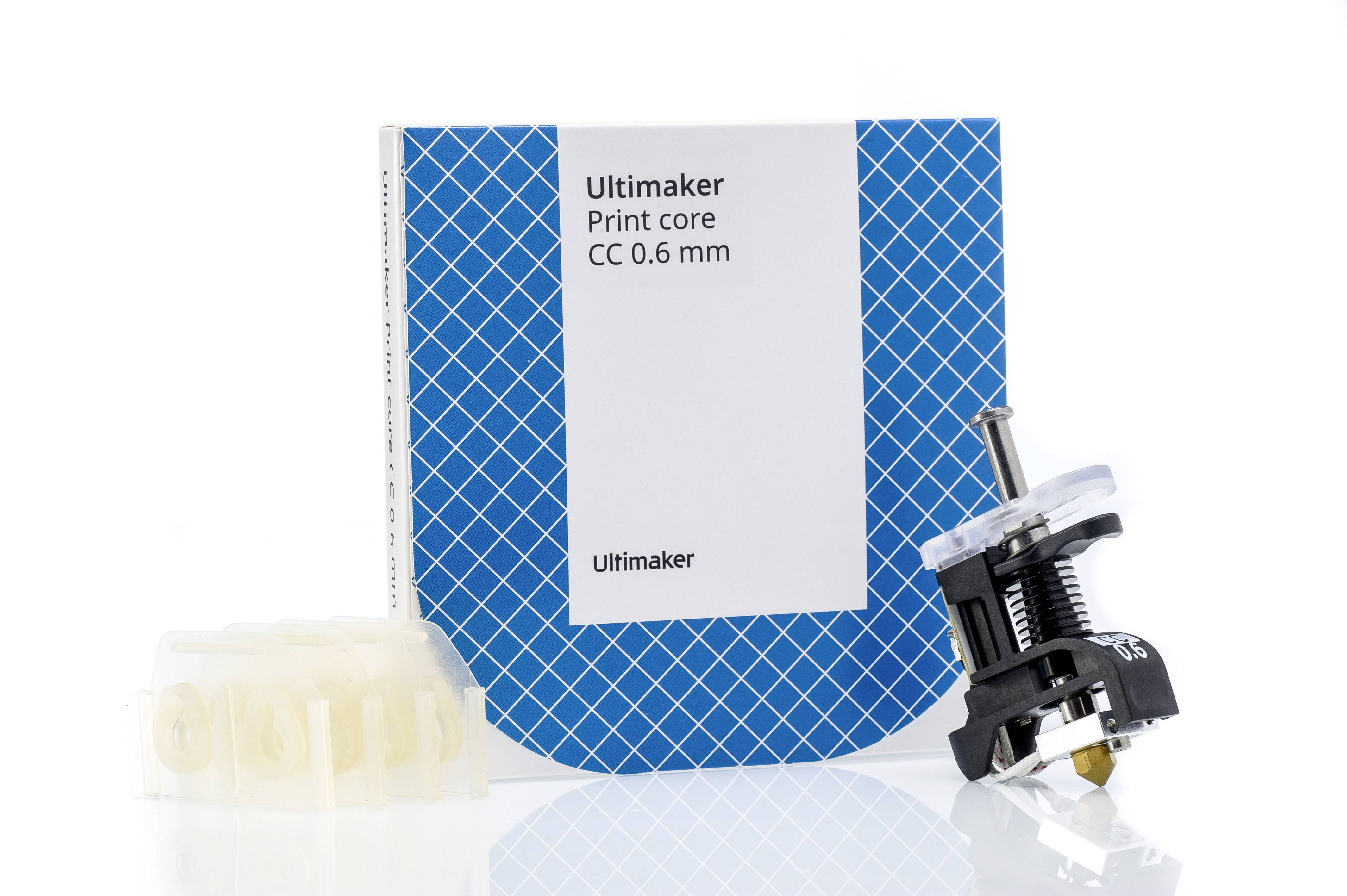 Dysza Ultimaker CC 0,6 mm przed niebieskim opakowaniem z wzorem kratki, z bliska widoczna głowica drukująca po prawej stronie.