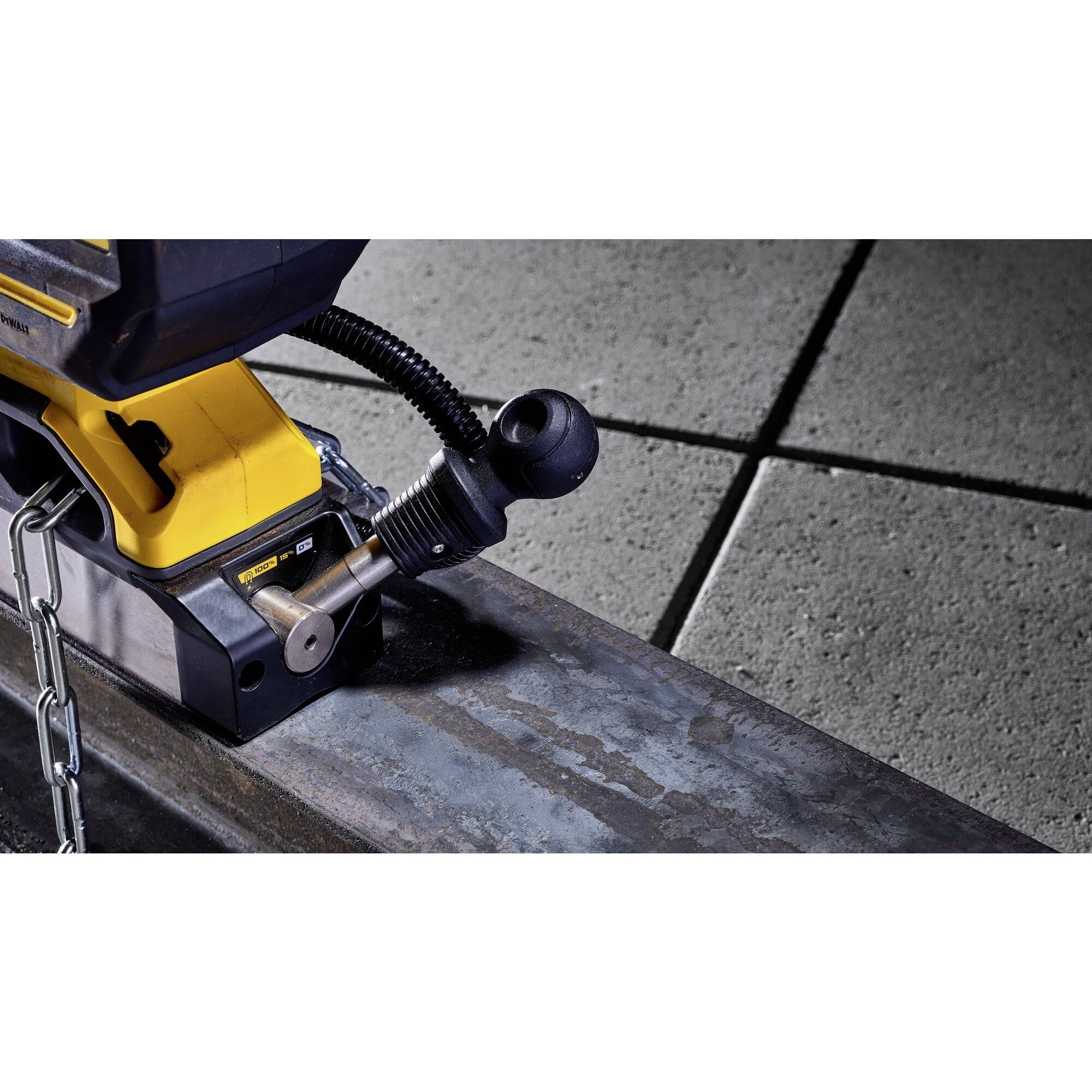 Zbliżenie żółtej maszyny obróbczej pracującej przy metalowym elemencie. Do urządzenia podłączony jest elastyczny wąż, a metalowe łańcuchy są widoczne.