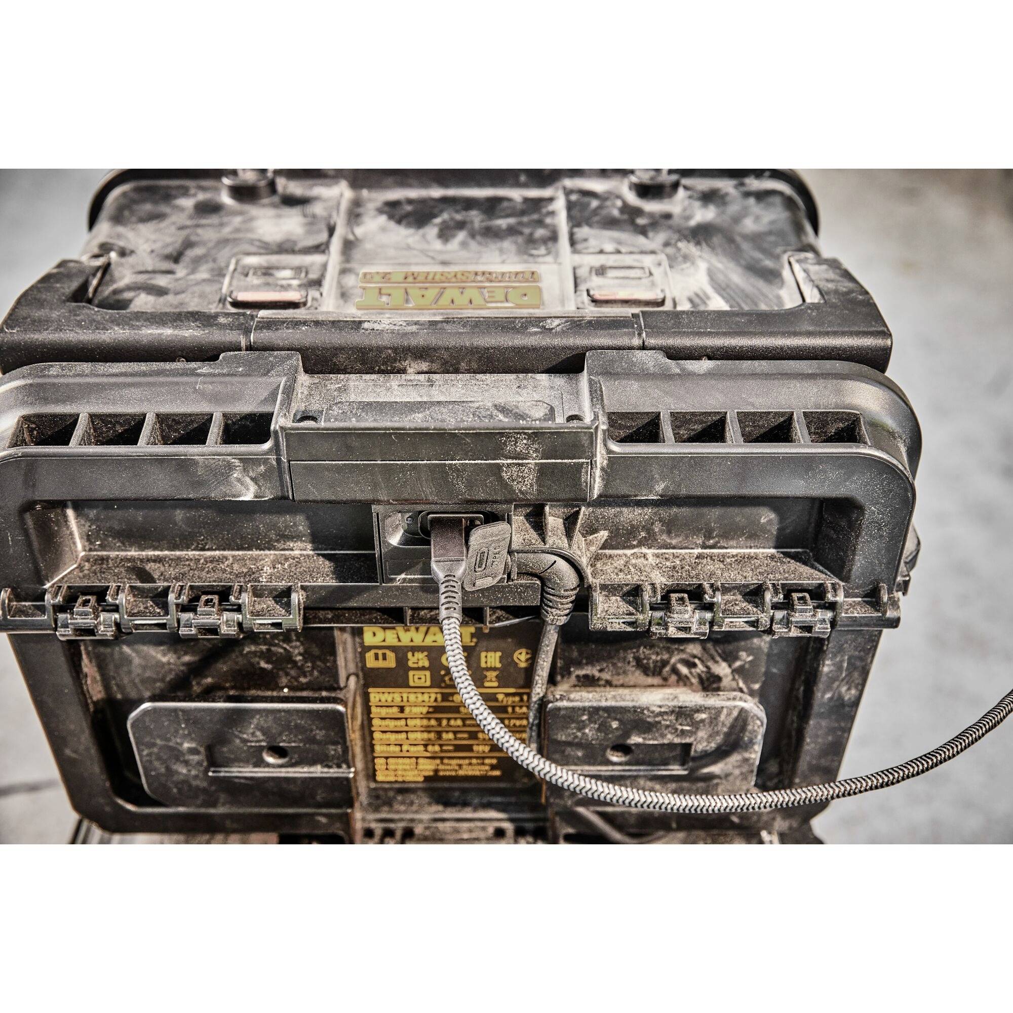 Brudna, czarna skrzynka narzędziowa z podłączonym przewodem elektrycznym stoi w warsztacie lub magazynie.