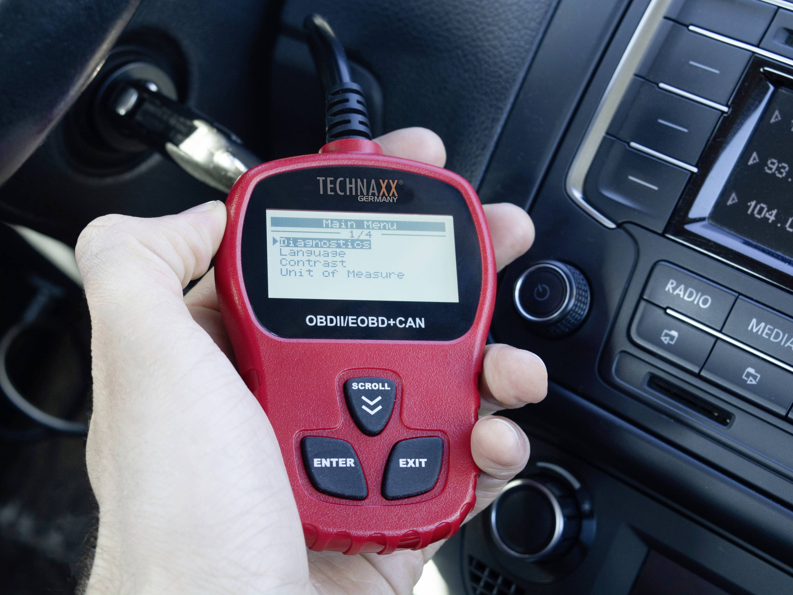 Osoba trzyma urządzenie diagnostyczne do samochodów, które jest podłączone do pojazdu. Na wyświetlaczu widoczne są opcje menu.