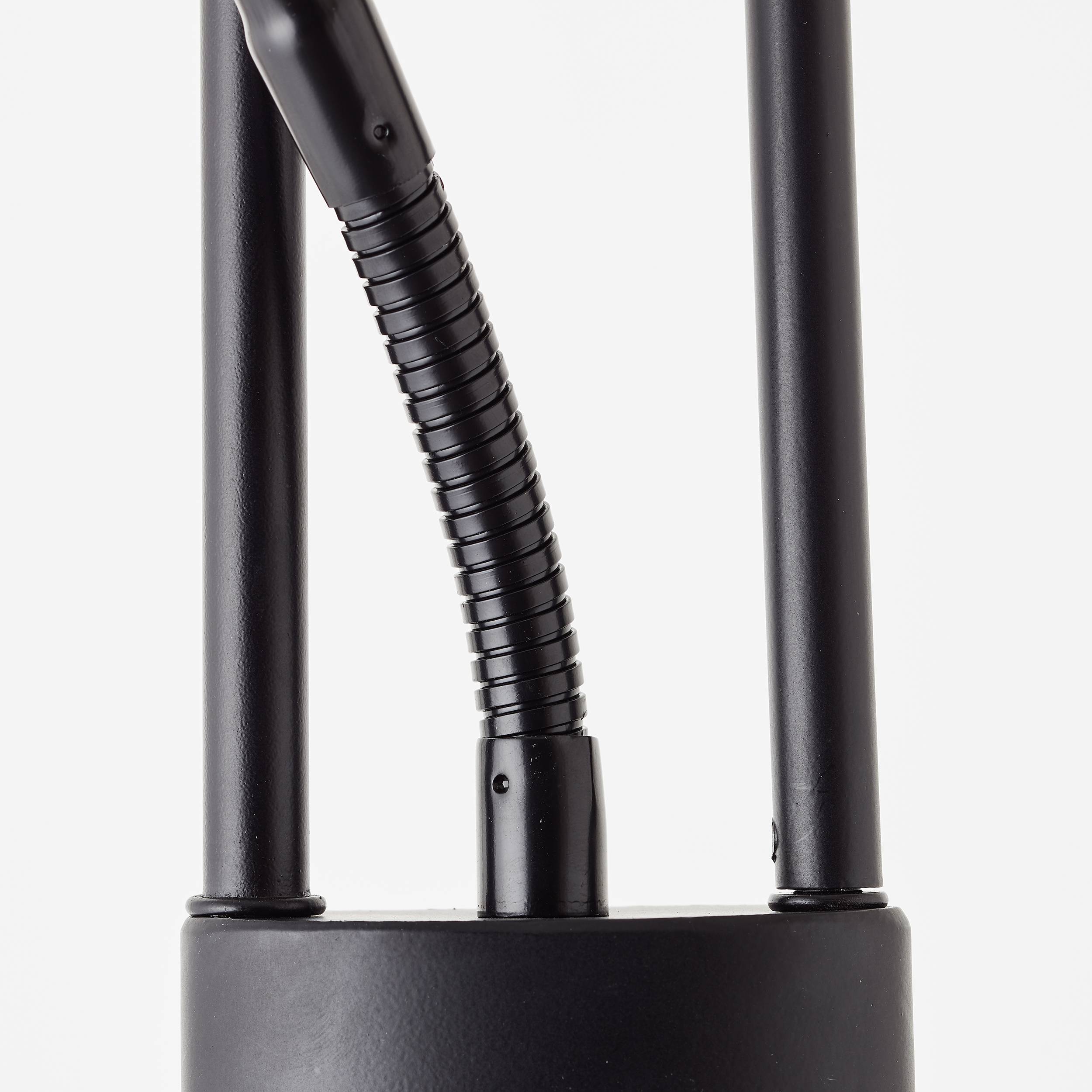 Czarny, cylindryczny obiekt z dwoma pionowymi prętami i elastycznym połączeniem pośrodku. Minimalistyczny, nowoczesny design.