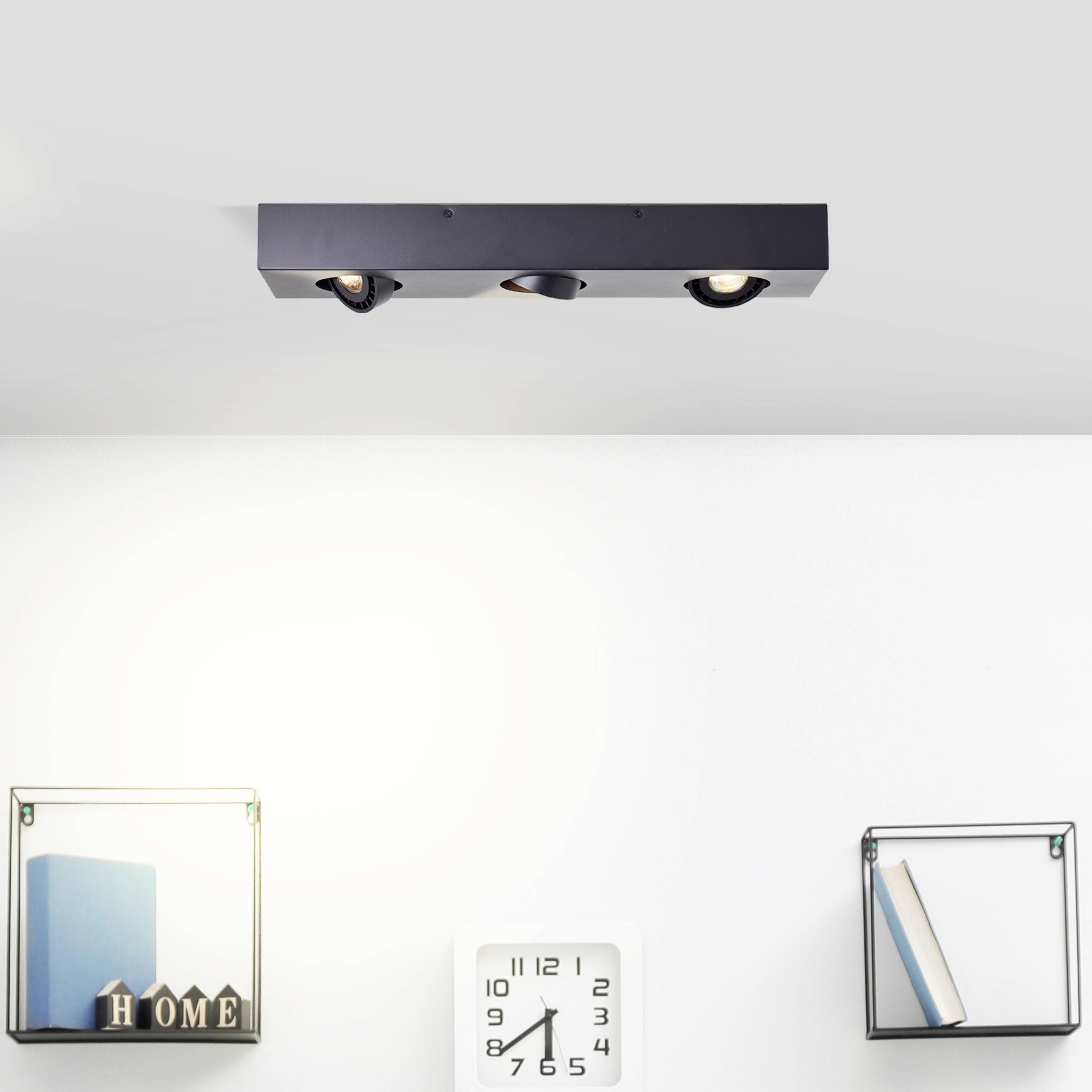 Lampa sufitowa z dwoma reflektorami, poniżej dwie półki z książkami i dekoracjami. Na środku ściany wisi zegar.