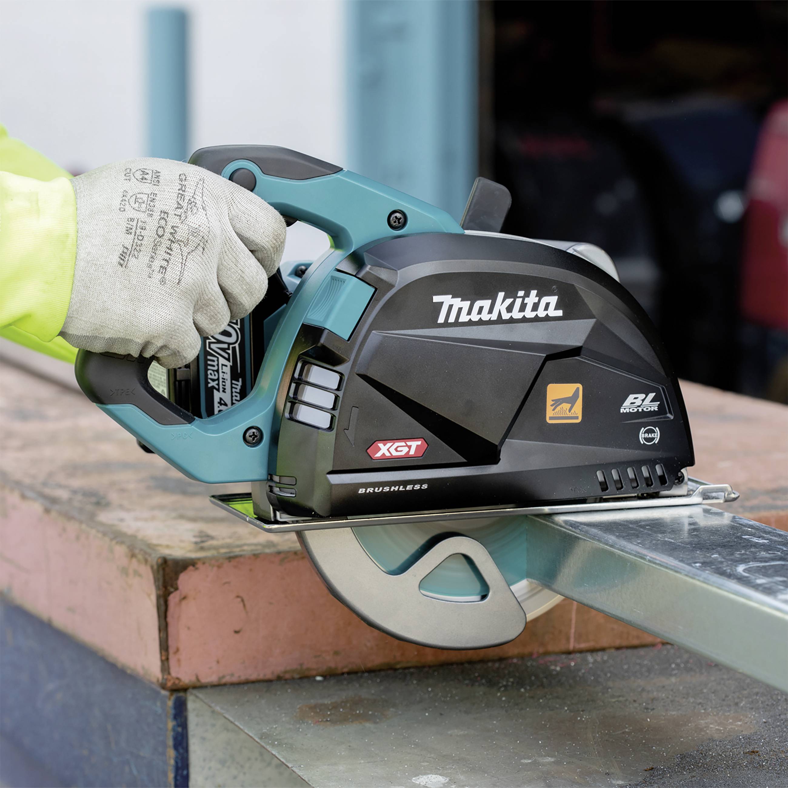 Osoba trzyma akumulatorową ręczną piłę tarczową marki Makita, która przecina drewno na placu budowy. Piła posiada oznaczenia 'XGT' i 'BL Motor'.