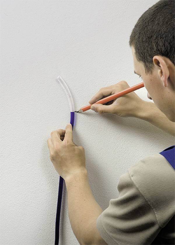 Osoba zagina kabel wokół ściany i zaznacza miejsce długopisem.