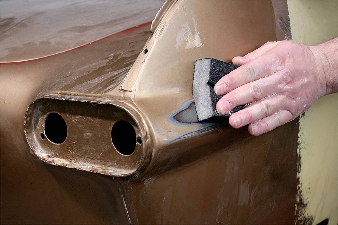 Ręka szlifuje zardzewiałą karoserię samochodu papierem ściernym.