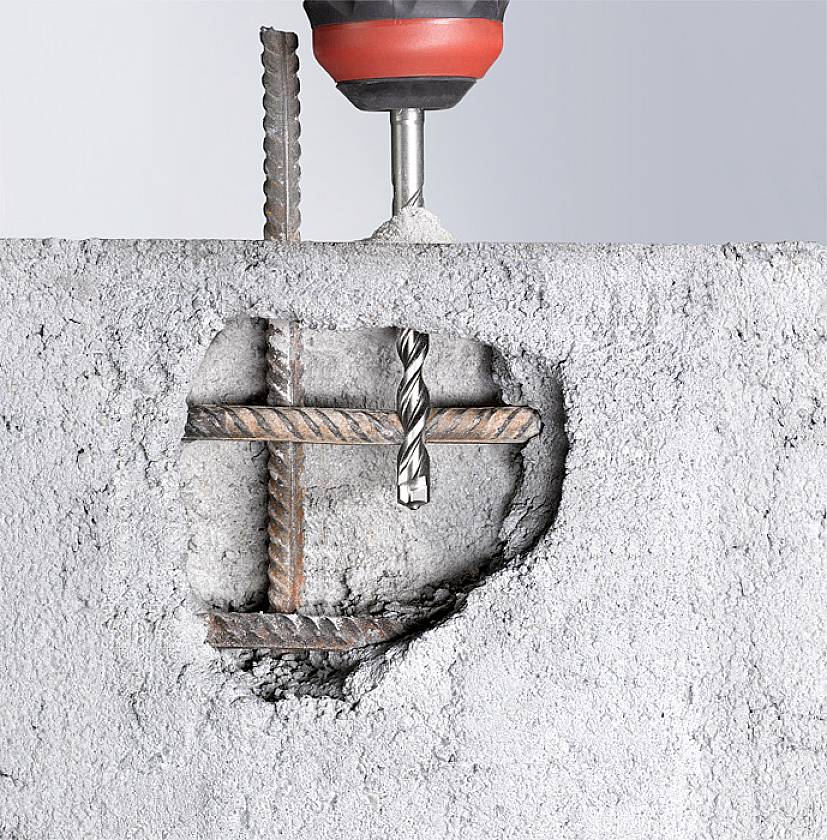 Wiertło przenika beton, odsłaniając wewnętrzne pręty zbrojeniowe. Symbolizuje siłę i technikę w budownictwie.