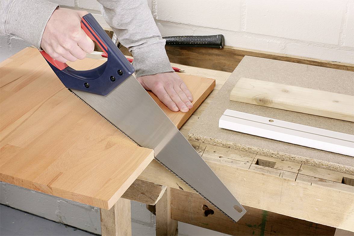 Osoba przecina drewnianą deskę na ławce warsztatowej.