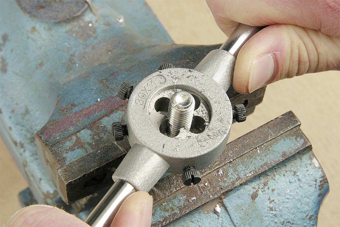 'Imadło trzyma pręt metalowy, podczas gdy gwintownik ręczny nacina gwint na pręcie. Dwie ręce prowadzą narzędzie.'