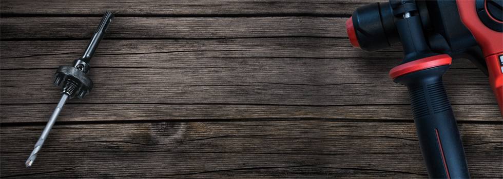 Akumulatorowa wiertarka z czerwonym uchwytem leży na drewnianym stole; obok znajduje się końcówka do wkręcania śrub.