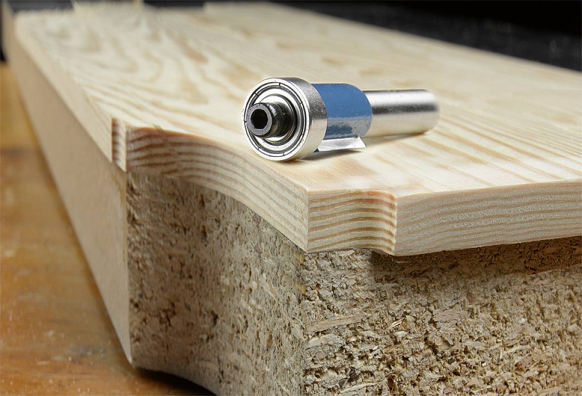 Frezarka leży na desce drewnianej, widoczna jest głowica frezarska. Idealna do prac frezarskich przy krawędziach i obróbce powierzchni.