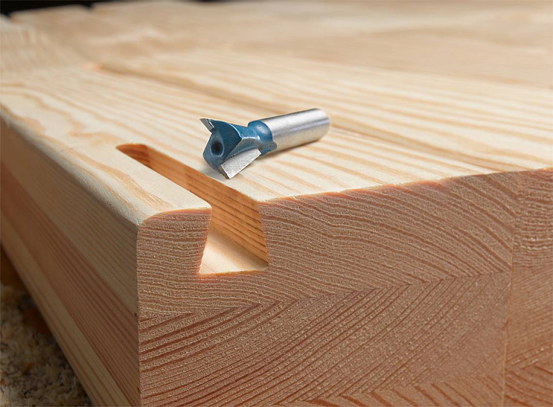 Frez na kawałku drewna z wyprofilowanym rowkiem; prezentuje proces obróbki drewna i narzędzie.