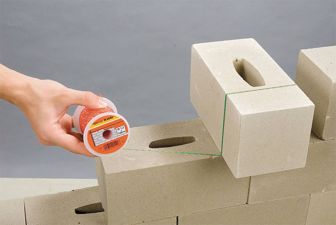 Osoba naciąga zieloną linę murarską nad ułożonymi blokami betonu komórkowego, aby oznaczyć prostą linię dla murowania.