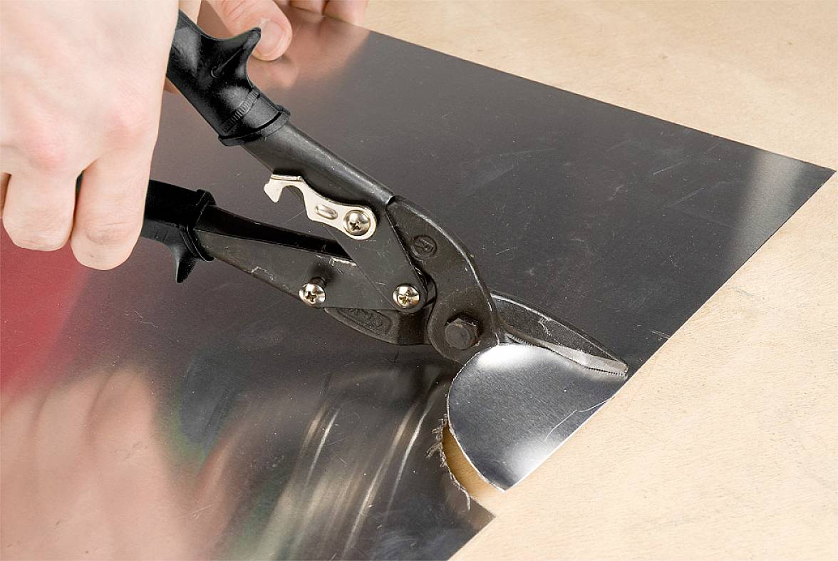 Osoba przecina kawałek aluminium nożycami do blachy. Ręce trzymają nożyce, precyzyjnie rozcinając metal.